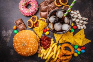 垃圾食品的概念。不健康的食物背景。快餐和糖。汉堡，糖果，薯条，巧克力，甜甜圈，苏打水，黑色背景。