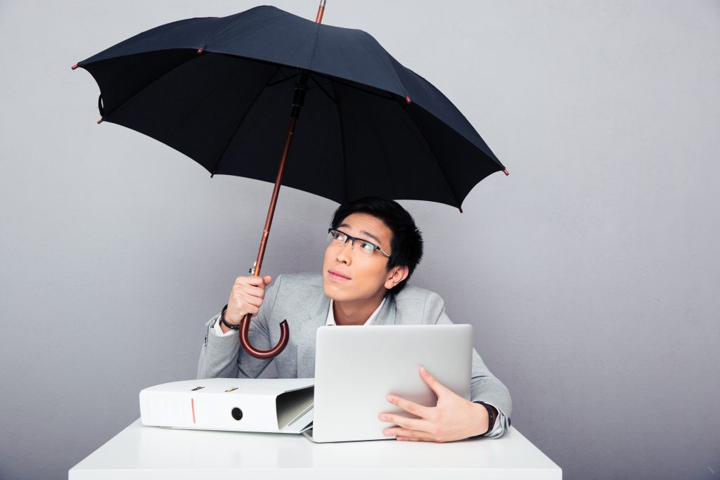 一名男子把笔记本电脑放在雨伞下的桌子上