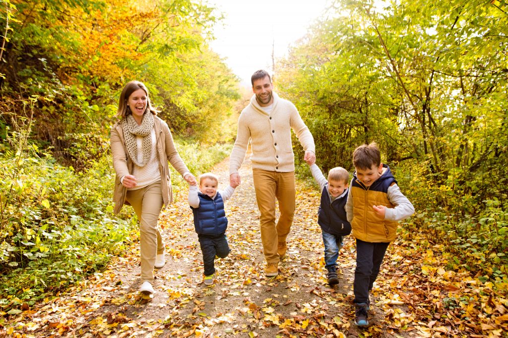 美丽年轻的家庭在森林散步。和他们的三个儿子的母亲和父亲在暖和的衣服在外面丰富多彩的秋天大自然。