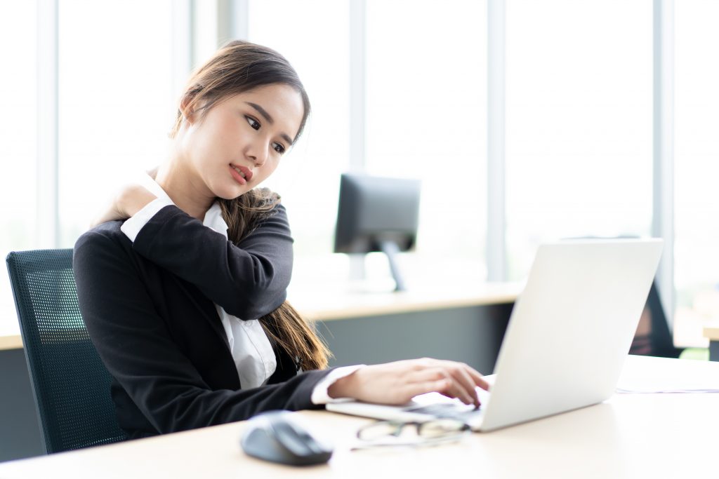 一位肩痛的女士在办公桌上用笔记本电脑工作。