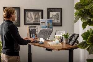 男子在站立式办公桌上工作，看着一台笔记本电脑在Goldtouch笔记本电脑/平板电脑的支架上。manbetx万博app下载使用Goldtomanbetx万博app下载uch FlexMouse和Goldtouch Go!2移动键盘