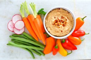 Hummus dip with a variety of fresh vegetables, above view on a white marble background. Healthy snack.