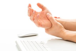 工作过度——患有腕管综合症——一名年轻男子因长时间在白色背景下使用键盘和鼠标而痛苦地握着手腕。